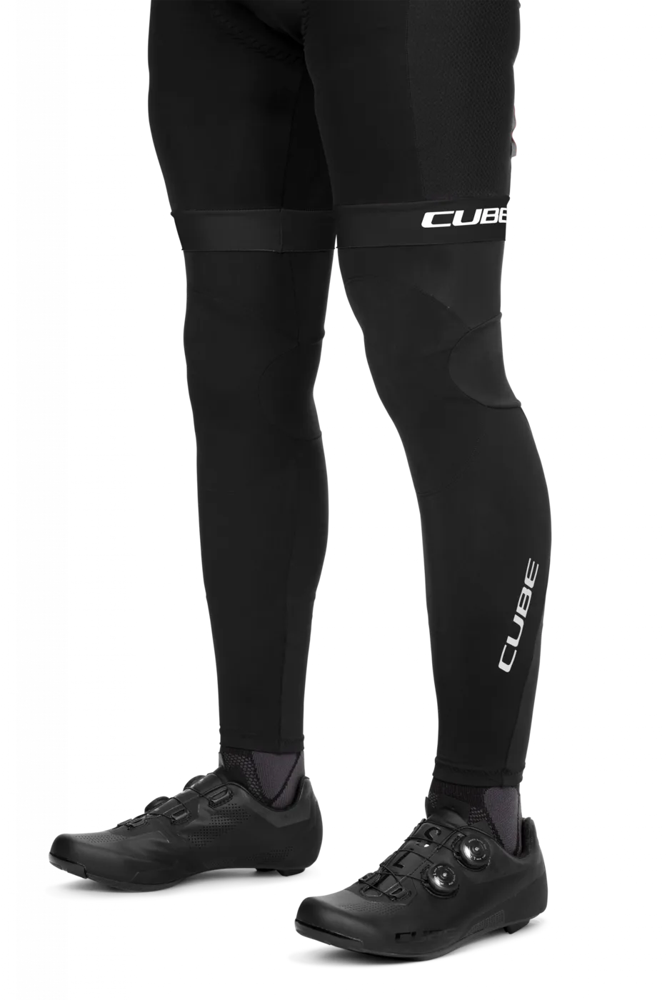 Eine Person trägt CUBE BLACKLINE Beinlinge und schwarze Fahrradschuhe, wobei "CUBE" auf den Beinlingen und Schienbeinen zu sehen ist. Die Unterschenkel und Füße sind vor einem weißen Hintergrund abgebildet.