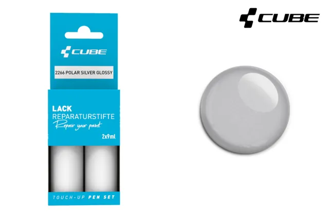 Das CUBE Lackstift Set POLAR SILBER glänzend 2266, abgebildet in blauer Verpackung neben einem passenden silbernen Lackmuster, ist perfekt für Mr. Bike Lichtenfels Fans. Das CUBE-Logo befindet sich in der rechten oberen Ecke.